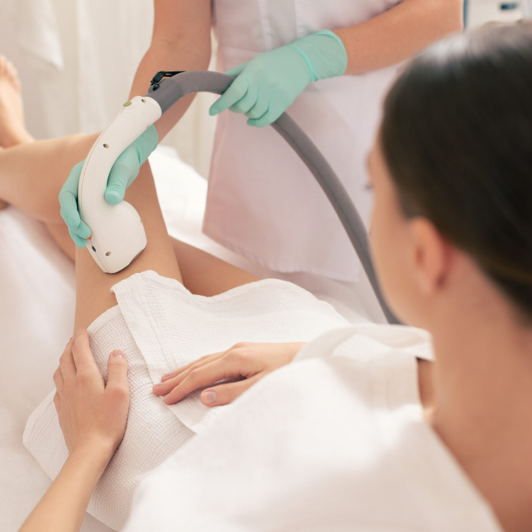 Woman in white bathrobe sitting on the medical couch and undergoing laser hair removal with a vacuum suction